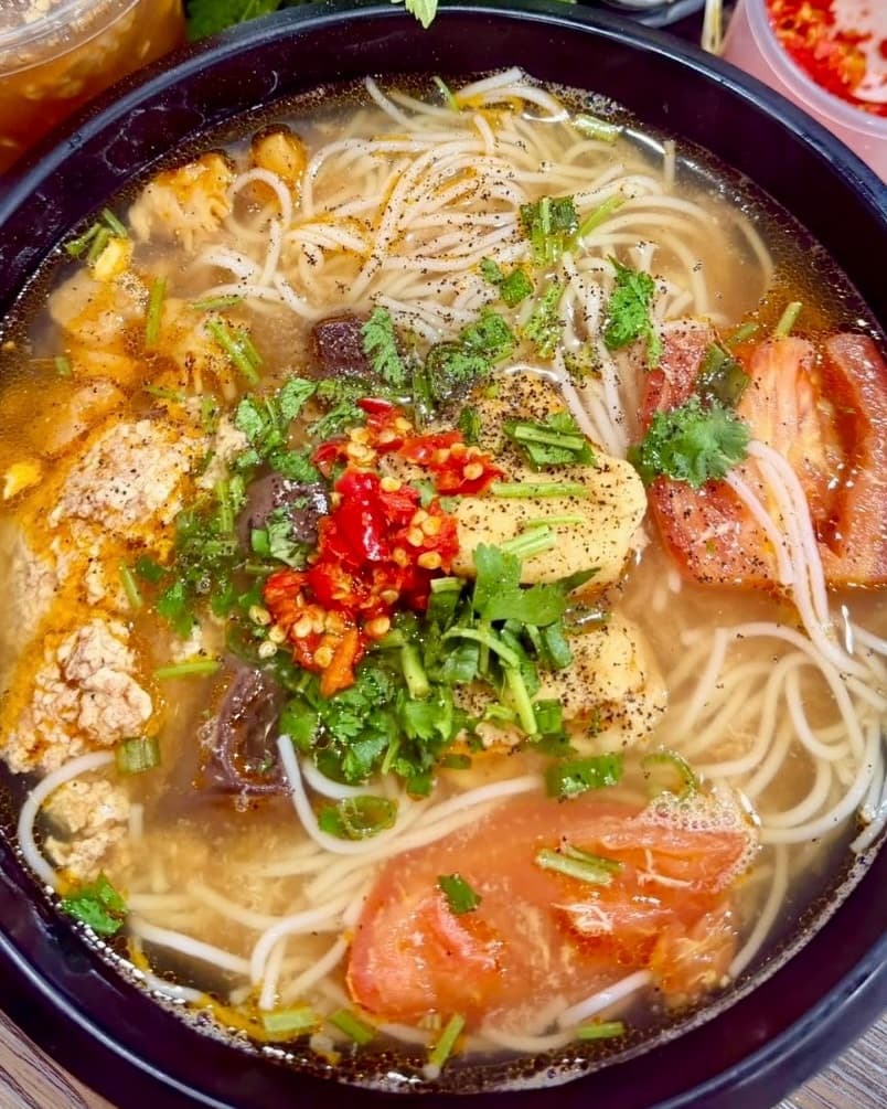 A bowl of Bún Riêu: crab and tomato soup with vermicelli, fresh chili, and herbs